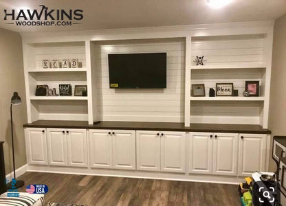 Wall-to-wall custom built-in entertainment center with white shiplap back panel, open display bookshelves, mounted TV, raised panel cabinet doors, and dark wood countertop, handcrafted made to order in the USA by Hawkins Woodshop
