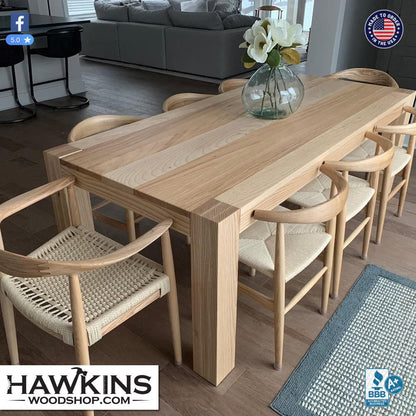 Modern white oak dining table with a thick solid wood top and chunky square legs, surrounded by light oak wishbone style chairs with woven paper cord seats, made to order in the USA by Hawkins Woodshop