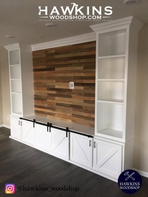 Custom built-in entertainment center by Hawkins Woodshop with white shaker cabinets, sliding barn doors, reclaimed wood accent media wall, and tall white bookcase towers, handcrafted and made to order in the USA