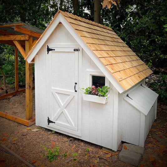 White wooden shed with a thatched roof in a garden setting
