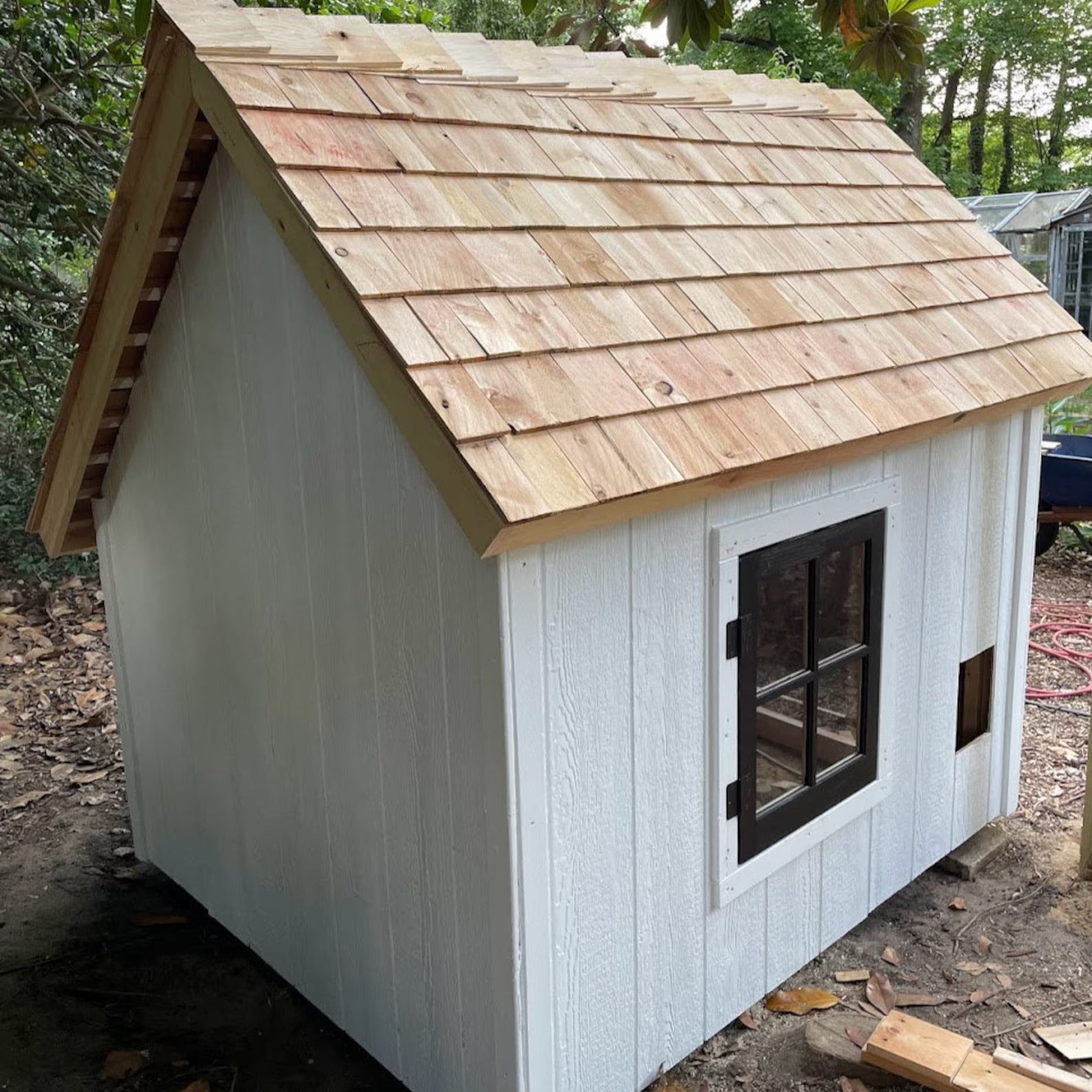 Small wooden cabin with a shingled roof in a forest setting